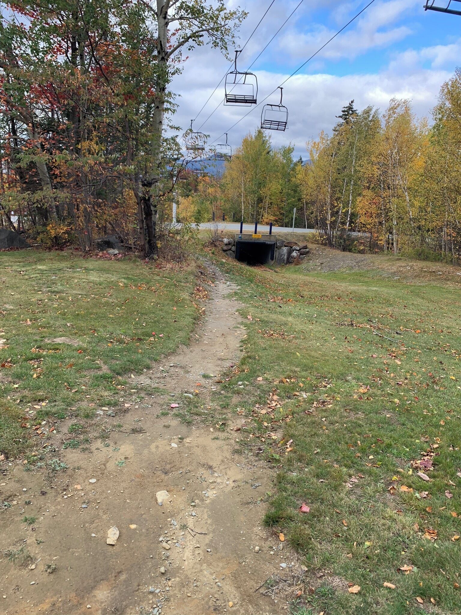 Un sentier de terre mène à l’entrée d’un tunnel, qui est entouré d’arbres aux feuilles d’automne.