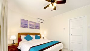 A hotel room with a bed, two bedside lamps, a ceiling fan, and a door. - Aloe Condo Arena at Eagle Beach (Noord)