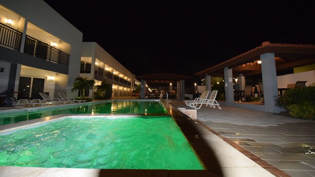 A swimming pool with lounge chairs and a covered seating area at night. - Aloe Condo Arena at Eagle Beach (Noord)