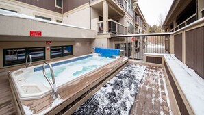 Een hottubgedeelte met een houten terras en sneeuw op de grond.