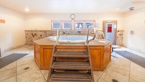 Een wellnessruimte met een houten bank, een bubbelbad en een stenen muur.
