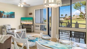 A dining area with a table set for four, a ceiling fan, and a large window with a view of a residential area.
