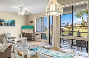 A dining area with a table set for four, a ceiling fan, and a large window with a view of a residential area.