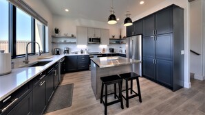 Une cuisine moderne avec des meubles de couleur sombre, des appareils en acier inoxydable et un grand îlot central doté de tabourets.