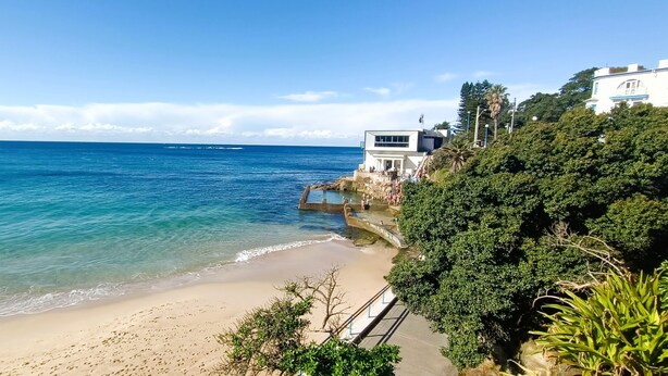 A beach with clear blue water, a sandy shore, and a modern building with a balcony overlooking the sea. - Watch The Sunrise Over Coogee | 2 Bedrooms + Garage (Coogee)
