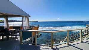 A deck with a railing overlooking the ocean, a table with chairs, and a view of the sea. - Watch The Sunrise Over Coogee | 2 Bedrooms + Garage (Coogee)
