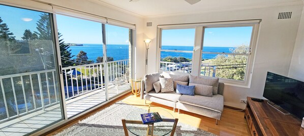 Ein Wohnzimmer mit einer Couch, einem Fernseher und großen Fenstern mit Meerblick.