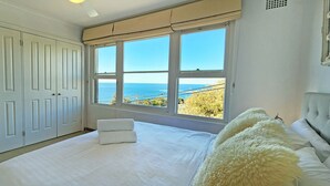A bedroom with a large bed, a window with a view of the sea, and a wardrobe. - Watch The Sunrise Over Coogee | 2 Bedrooms + Garage (Coogee)