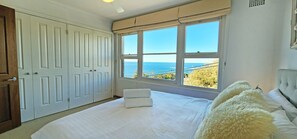 Une chambre avec un grand lit, une fenêtre donnant sur la mer et une armoire.