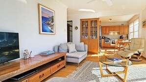 A modern living room with a sofa, a glass coffee table, a TV, and a wooden entertainment unit. - Watch The Sunrise Over Coogee | 2 Bedrooms + Garage (Coogee)