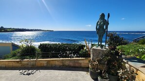 A coastal view with a statue on a pedestal, overlooking the sea and a distant shoreline with buildings. - Watch The Sunrise Over Coogee | 2 Bedrooms + Garage (Coogee)