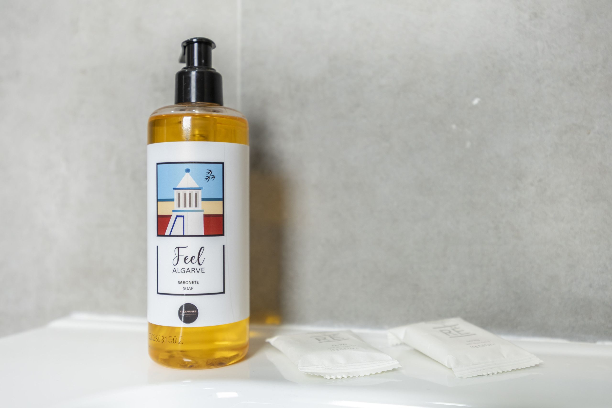 A bottle of soap with a pump dispenser, a label with a building illustration, and two packets of soap on a white surface.