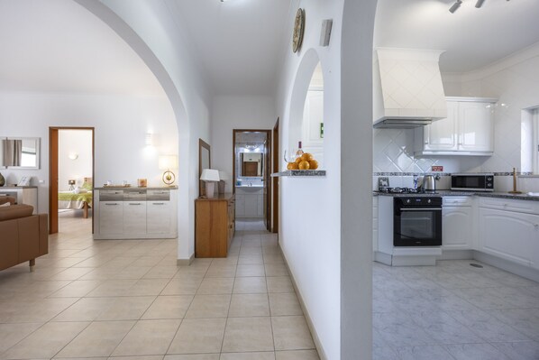 A spacious living area with a sofa, a wooden cabinet, and a kitchen with a stove and cabinets.