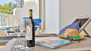Ein Tisch mit einer Weinflasche, zwei Gläsern, einem Buch und einem Strohhut vor einem Gebäude.