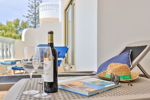 A table with a bottle of wine, two glasses, a book, and a straw hat on a metal table outside a building. - CoolHouses Algarve Luz | Blue Ocean View T2 (Luz)