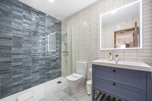 A modern bathroom with a glass shower enclosure, a toilet, and a vanity with a mirror. - CoolHouses Algarve Luz | Blue Ocean View T2 (Luz)