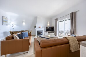 A modern living room with a fireplace, a television, and a dining area. - CoolHouses Algarve Luz | Blue Ocean View T2 (Luz)