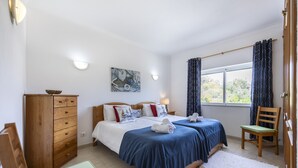 Ein Hotelzimmer mit zwei Betten, einem Holzkleiderschrank, einem Schreibtisch, einem Stuhl und einem Fenster mit Vorhängen.