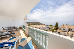 A balcony with lounge chairs, a table, and a view of a coastal town. - CoolHouses Algarve Luz | Blue Ocean View T2 (Luz)