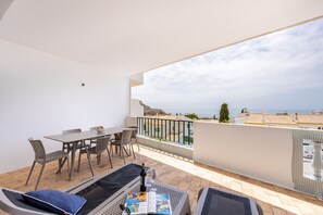 A balcony with a table and chairs, a sofa, and a view of the sea.