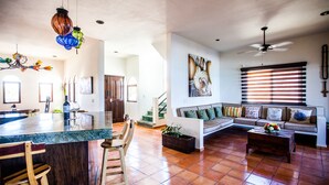 A spacious living room with a large sofa, a coffee table, and a kitchen area with a bar and chairs. - Casa Nido del Gallo Solar Ocean Front Deluxe Home 3 bedrooms, 5 bathrooms (Isla Mujeres)