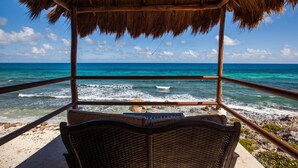 A beach view from a thatched-roof structure with a wicker chair in the foreground. - Casa Nido del Gallo Solar Ocean Front Deluxe Home 3 bedrooms, 5 bathrooms (Isla Mujeres)