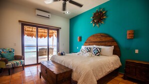 A bedroom with a large bed, a wooden headboard, a bench, and a view of the ocean through a sliding door. - Casa Nido del Gallo Solar Ocean Front Deluxe Home 3 bedrooms, 5 bathrooms (Isla Mujeres)