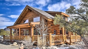 A log cabin with a porch, a car parked in front, and a mountainous backdrop. - Riverfront Retreat w/ Hot Tub: Fish & Hike! (Buena Vista)