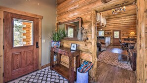 A log cabin interior with a wooden door, a mirror above a console table, a staircase leading to an upper level, and a dining area with a chandelier. - Riverfront Retreat w/ Hot Tub: Fish & Hike! (Buena Vista)