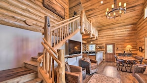 A log cabin interior with a wooden staircase, leather sofas, a dining area, and a kitchen. - Riverfront Retreat w/ Hot Tub: Fish & Hike! (Buena Vista)