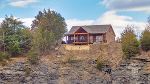 Een vakantiehuis met een veranda, gelegen op een rotsachtige klif omringd door bomen.