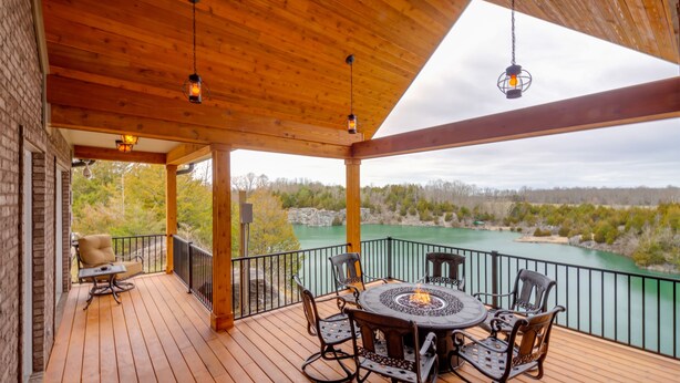 Een houten terras met een ronde tafel en stoelen, uitkijkend op water en bomen.