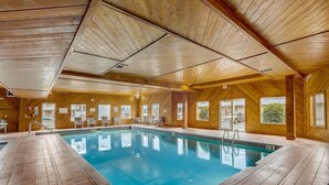 A large indoor swimming pool with wooden walls and ceiling, surrounded by lounge chairs and a tiled floor.