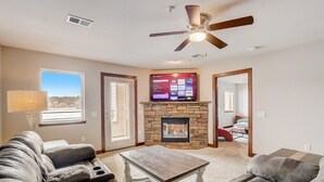 A living room with a stone fireplace, a flat-screen TV mounted above it, and a ceiling fan.