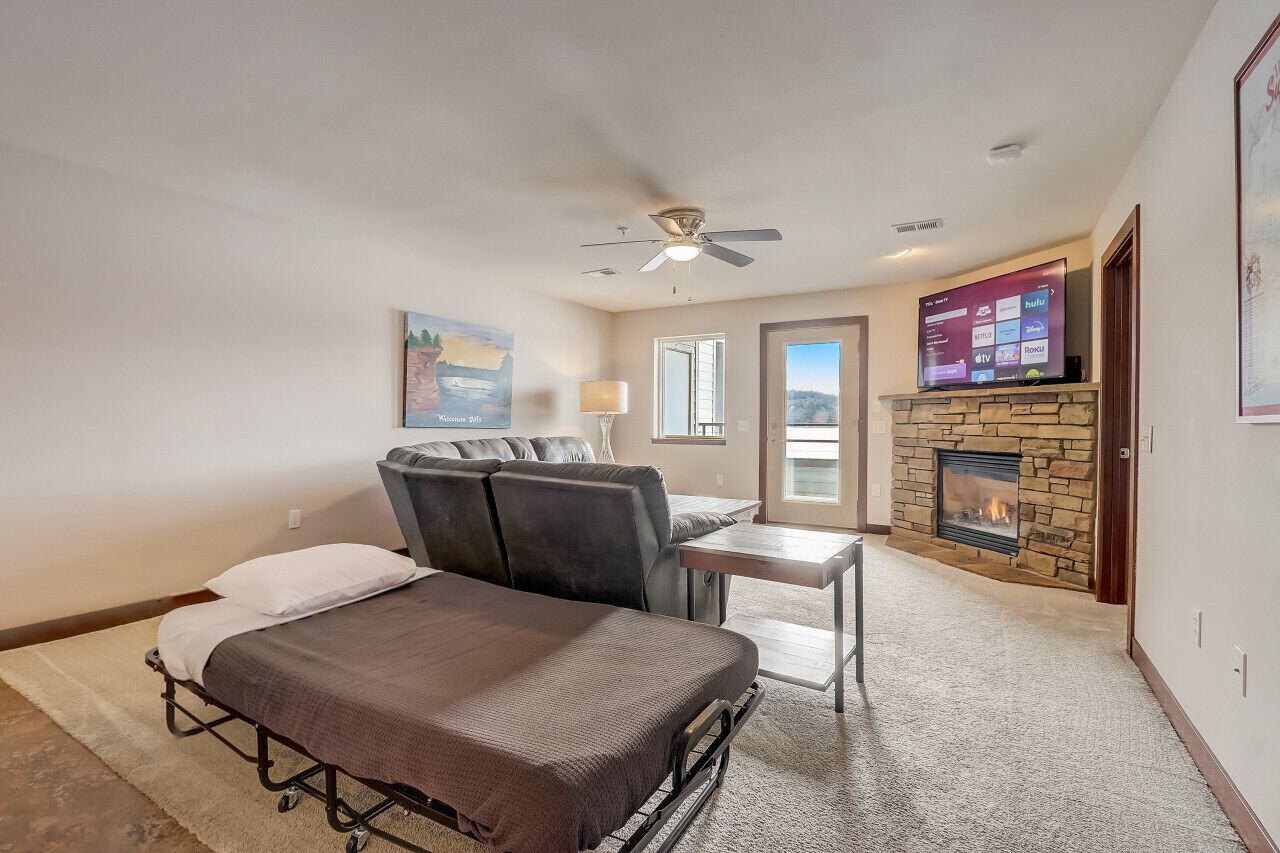 A bedroom with a bed, a sofa, a TV, a fireplace, and a ceiling fan.
