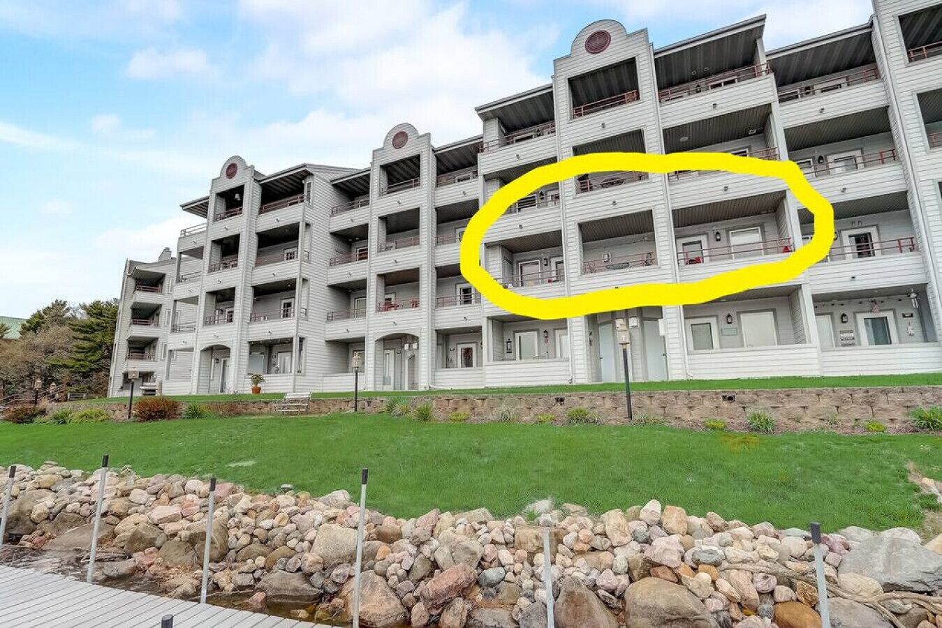 A multi-story hotel with a symmetrical facade, balconies on each floor, and a stone retaining wall in the foreground.