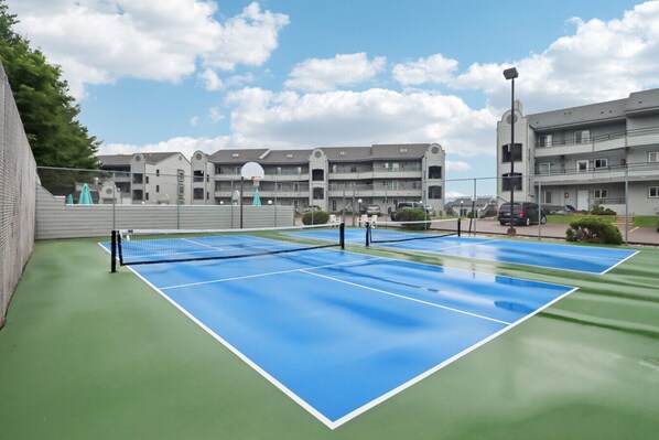 En utomhusbana för tennis med ett nät i mitten, omgiven av en grön yta.