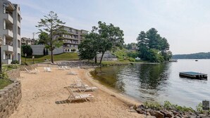 A lakeside resort with a sandy beach, lounge chairs, and a dock.