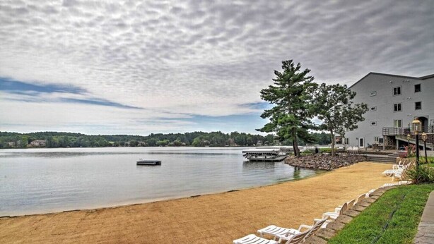 A lakeside hotel with a sandy beach, lounge chairs, and a dock.