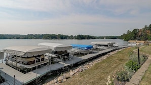 A dock with covered boat storage, a grassy area, and a view of a lake with trees in the background.