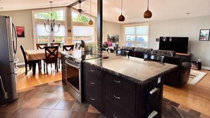 A spacious kitchen with a large island, dark cabinetry, and a dining area with a table and chairs. - Oak Street Cottage - 3BRM with Backyard Retreat (Prince Edward)