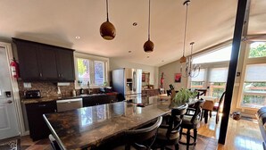 A modern kitchen with a large island, dark cabinets, and pendant lighting. - Oak Street Cottage - 3BRM with Backyard Retreat (Prince Edward)