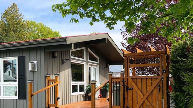 A two-story building with a wooden deck, a gated entrance, and a small porch area. - Oak Street Cottage - 3BRM with Backyard Retreat (Prince Edward)