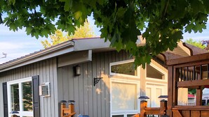 A small, single-story building with a wooden deck, a gated entrance, and a staircase leading to the door. - Oak Street Cottage - 3BRM with Backyard Retreat (Prince Edward)