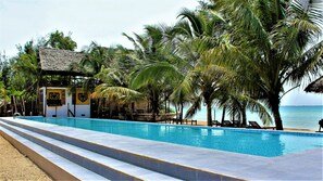 A swimming pool with steps leading into it, surrounded by palm trees and a beach. - Asante Sana Beach Cottages - Beachfront Cottage  (Fukuchani)