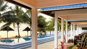 Ein Poolbereich am Strand mit einer Liege, einem Tisch und Blick auf den Strand und den Ozean.