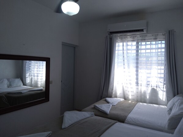 Une chambre d’hôtel équipée d’un lit, d’un miroir, d’un appareil de climatisation et d’une fenêtre avec des rideaux.