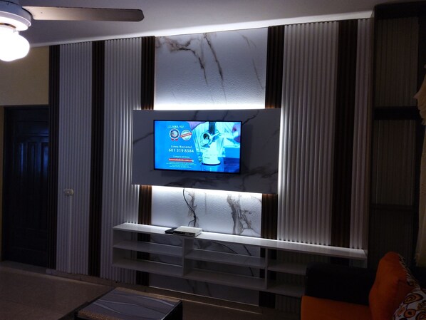 Un salon moderne doté d’un téléviseur à écran plat fixé sur un mur en marbre, d’un ventilateur de plafond et d’une étagère intégrée située sous le téléviseur.