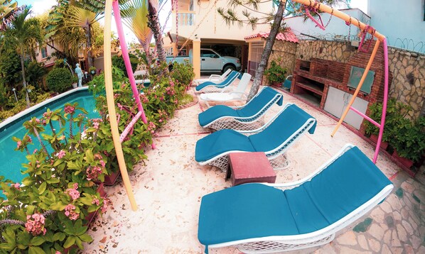 A poolside area with lounge chairs, a barbecue, and a stone wall.