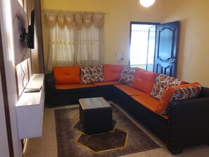 A living room with a sectional sofa, a coffee table, a television, and a window with curtains.